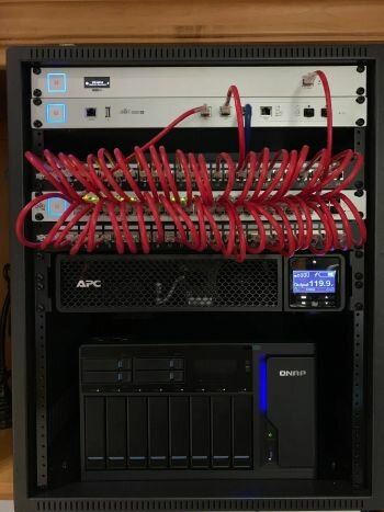 Serverrack med nätverksutrustning, kablar, UPS, och lagringsenhet inom IT-infrastruktur.