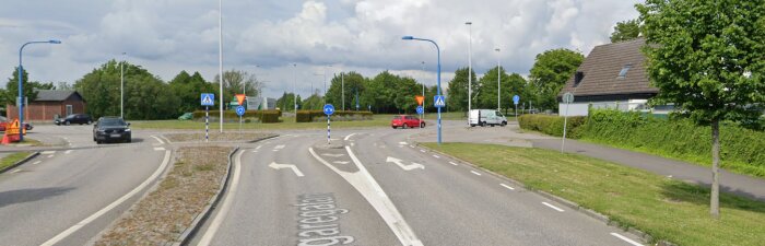 Svensk rondell med bilar, skyltar, och cykelbanevägvisning under en mullig himmel.