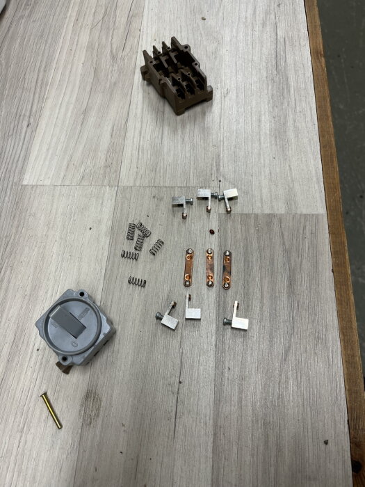 Elektriska komponenter och fjädrar noggrant organiserade på ljus träyta. Demontering eller reparation kan vara pågående.