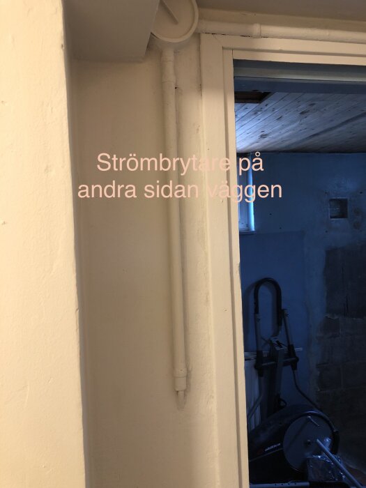 Vit dörrkarm, rör längs vägg, text: "Strömbrytare på andra sidan väggen", inblick i blått rum.