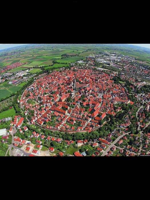 Flygfoto av en befäst stad med ringmur, omgiven av gröna fält och modernare områden.