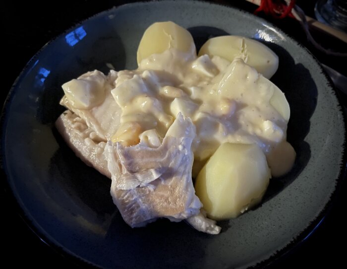 Kokt potatis, sås, troligen stuvad fisk, mörk tallrik, maträtt, hemlagad, traditionell måltid, enkel presentation.