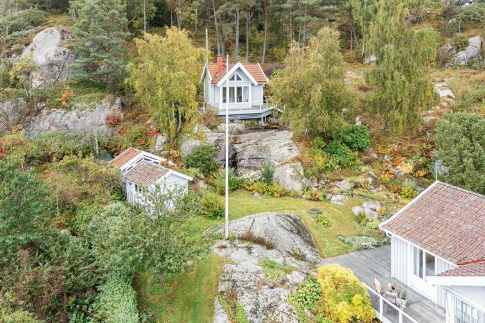 Vit villa omgiven av grönska och klippor, i skandinavisk miljö, höstfärger, vindlande trädgård, lugnt och fridfullt.