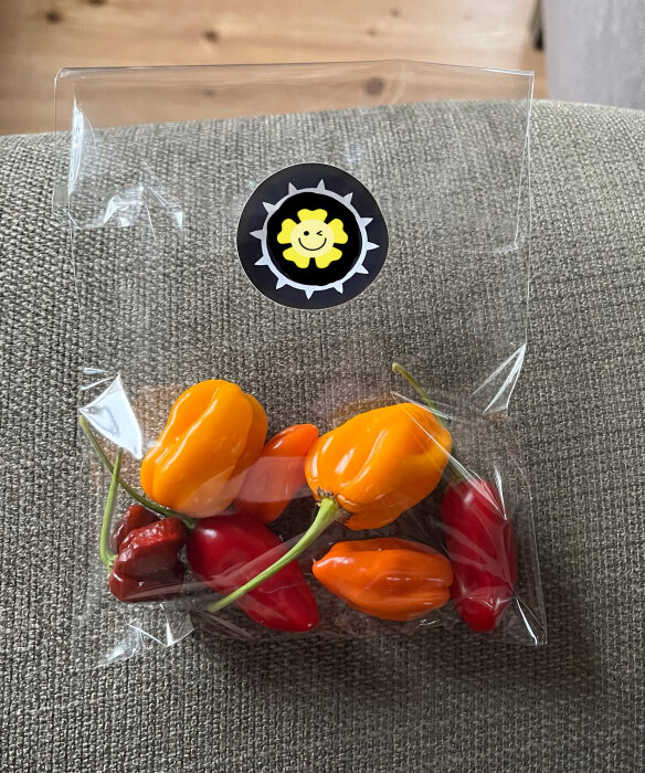 Genomskinlig förpackning med olika färgade chili på tygyta. Klistermärke med sol-liknande symbol ovanpå.