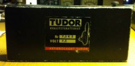 Svart TUDOR batteri, "Kvalitetsstartbatteri", Nr. 7,5 K 3, 7.5 volt, etikett med text, ligger på bord.