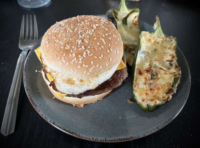 En cheeseburgare och grillade, fyllda paprikor på en mörk tallrik.