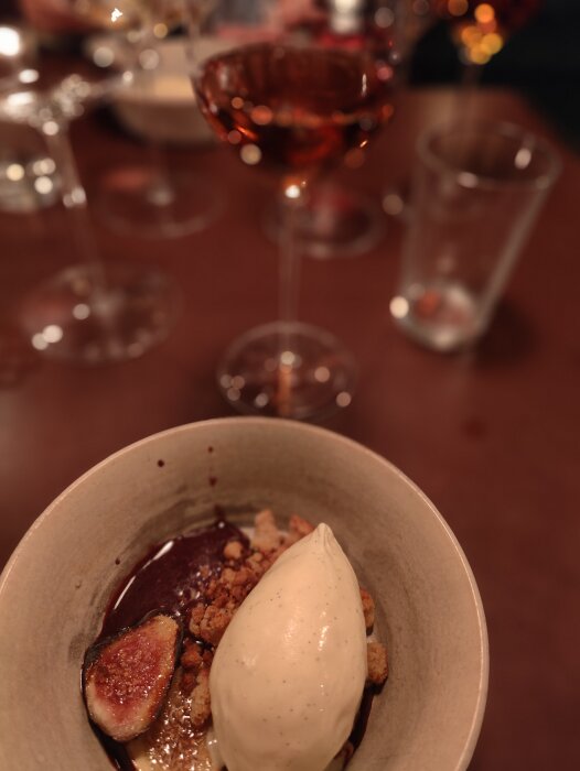 Efterrätt med fikon och glass, krispiga smulor, chokladsås, oskarp bakgrund med rosévin och tomma glas.