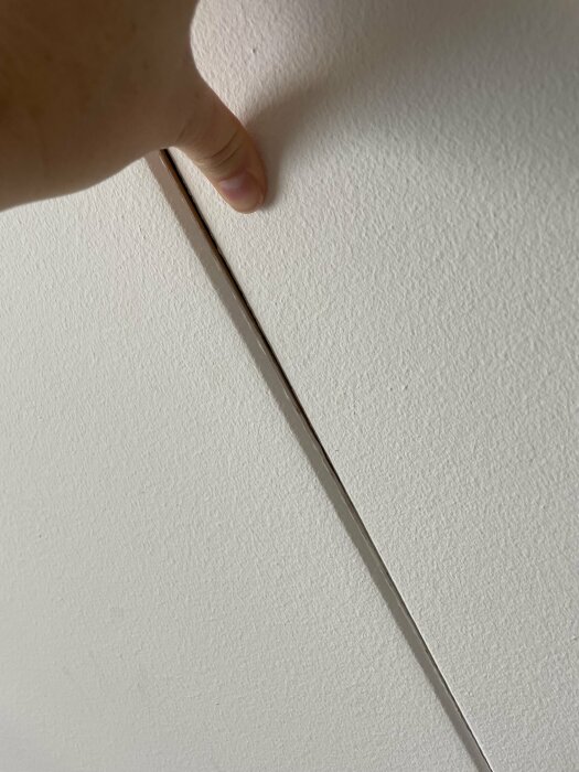 Hand trycker mot vit vägg, skapar skugga och illusion av ett gap.