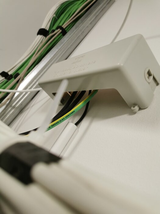 Vit kabelkanal på vägg med gröna och vita kablar.