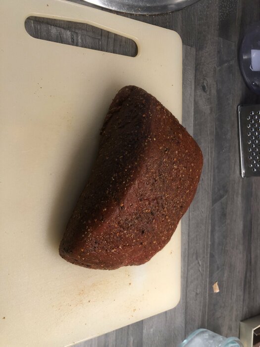 Ett bröd på skärbräda, mörkt, sesamfrön, köksmiljö, delvis skuret.