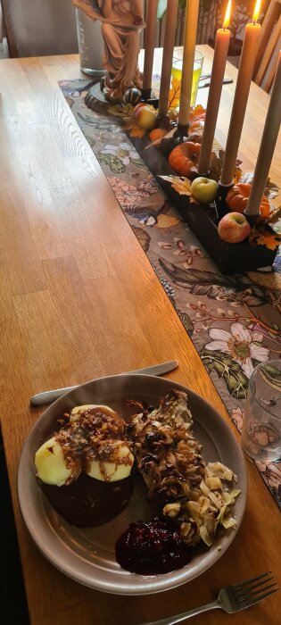 Mysig middagsmiljö med tända ljus, blommig duk, en mustig måltid, äpplen och en dekorativ figur.