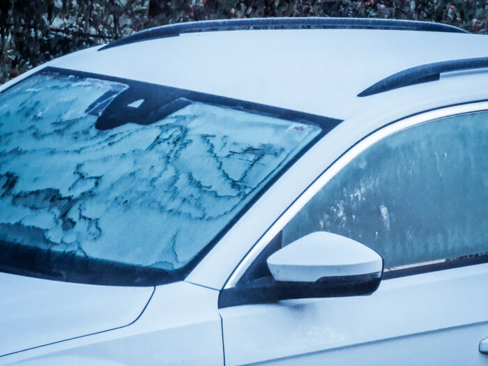 En snötäckt bil med isiga mönster på sidorutan under vinter-, eller kyligt, väder.