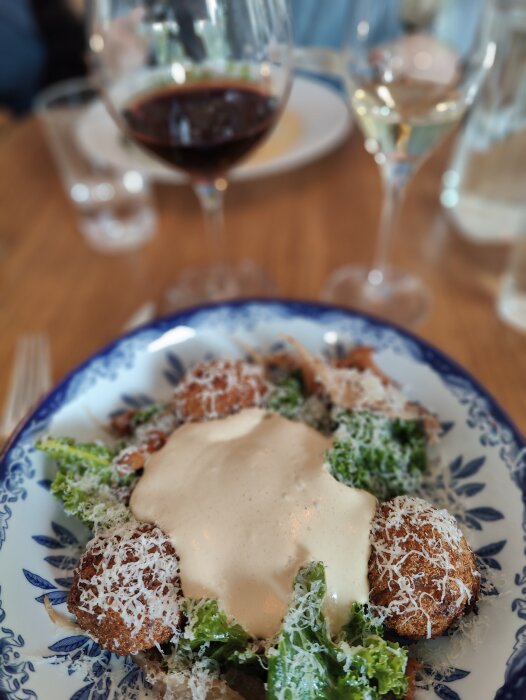 En sallad med dressing och riven ost, närbild, suddig bakgrund med röd och vitvin. Eleganta glas och tallrikar.