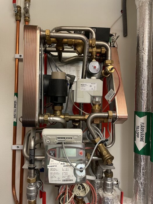 Komplex värmepumpsinstallation med rör, kablar, mätare och säkerhetsutrustning monterade på en vägg.