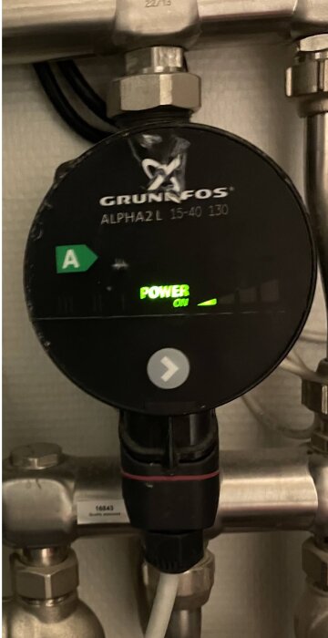 Cirkulationspump av märket Grundfos med påslagen status, inbyggd i ett rörsystem.