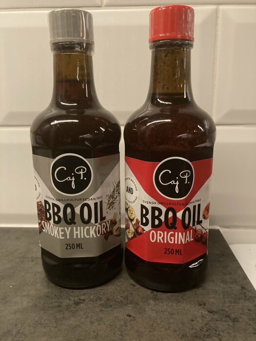 Två flaskor BBQ-olja, Smokey Hickory och Original, på köksbänk.