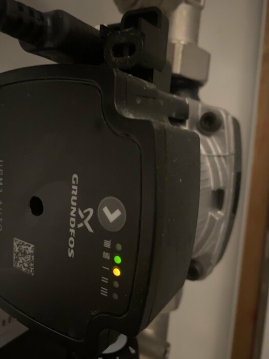 Cirkulationspump från Grundfos, indikeringslampor tända, kablar kopplade, del av rörsystem synligt.