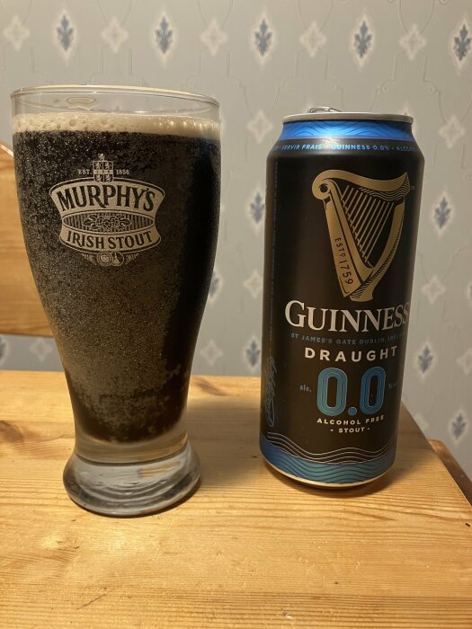 Ett glas mörkt öl bredvid en Guinness alkoholfri stoutburk på ett träbord.