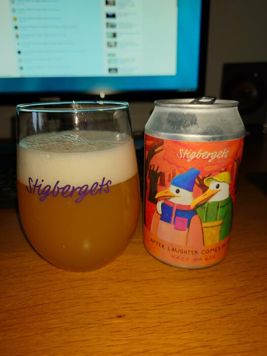 Ölglas fyllt med disig dryck, färgrik burk med konstnärlig design, text "Stigbergets", "After Laughter Comes... Hazy IPA".