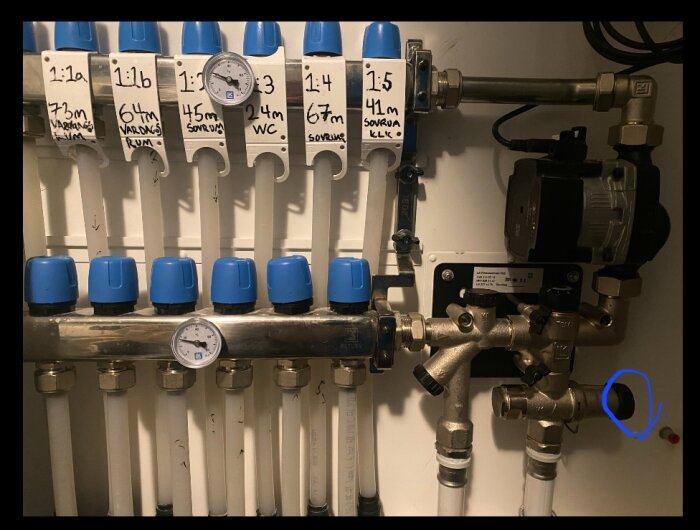 Värmerörsfördelare med manometer och etiketter för rum. Termostatventiler och cirkulationspump syns också.