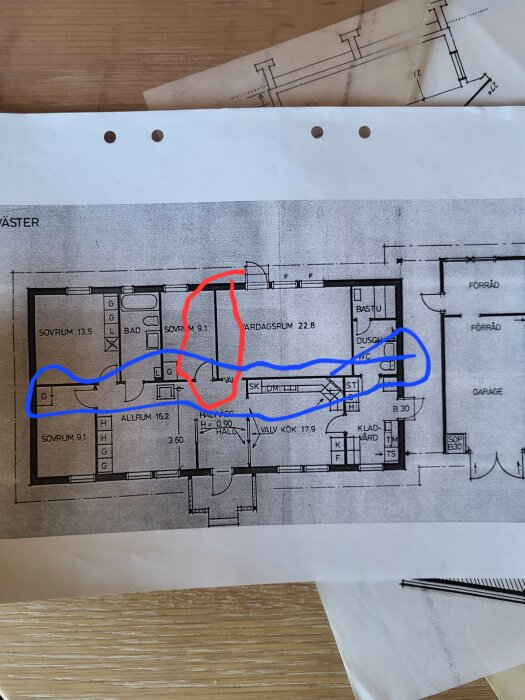Ritning av husplan med överstrukna linjer i rött och blått, arkitektoniska symboler, flera rum och måttangivelser.