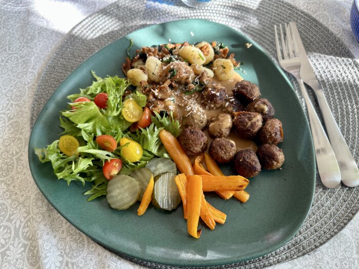 Tallrik med köttbullar, stekta potatisar, morötter, sallad och inlagda gurkor, komplett måltid.