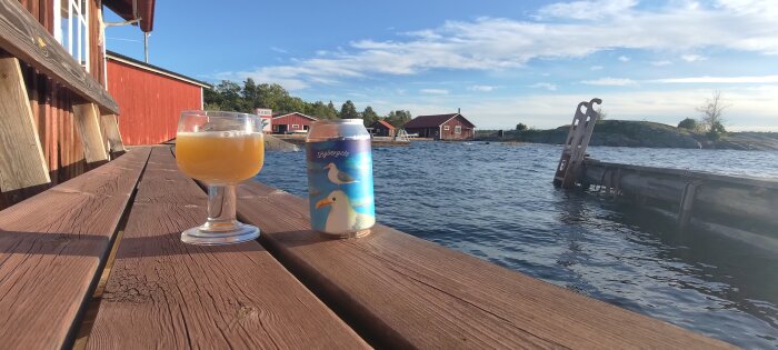 En dryck i glas, burk med sjömåsar, brygga, röda stugor, hav, klar himmel. Relaxande sommarstämning vid svensk skärgård.