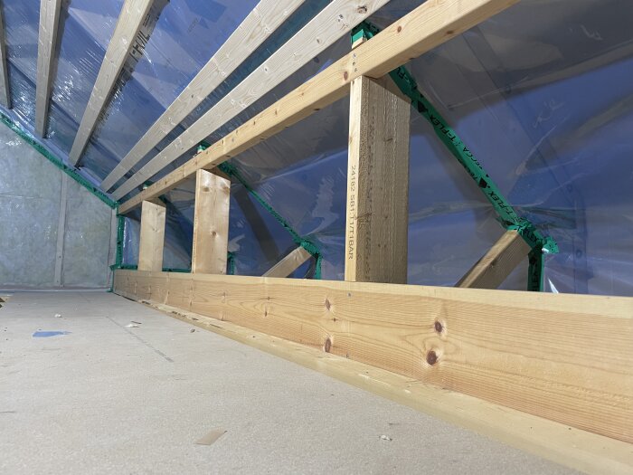 Inre takkonstruktion med träbjälkar, isolering och plastfolie synlig i ett pågående byggprojekt.