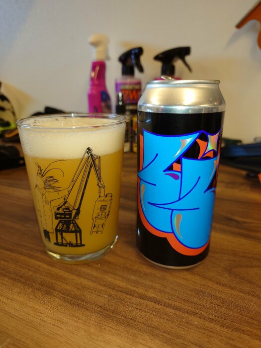 Ett glas öl och en färgglad burk på ett träbord med bakgrund av städprodukter.