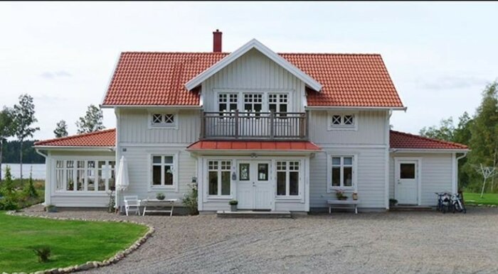 Tvåvåningshus, vit fasad, rött tak, veranda, balkong, grusgång, grönska, lugnt, traditionell stil, uteplats, cyklar.