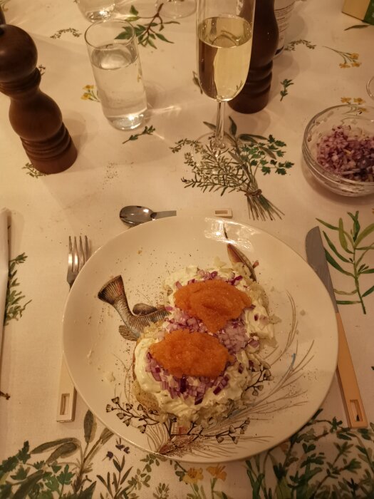 Maträtt med fiskrom, rödlök, gräddfil på knäckebröd, dukat bord, glas med vin och vatten.