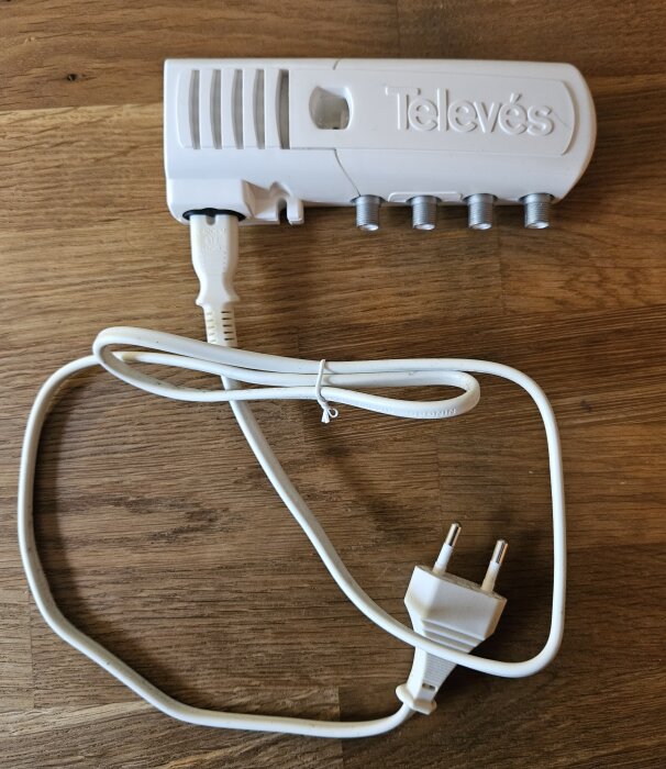 Vit TV-signal förstärkare med strömkabel och europeisk stickkontakt på träbakgrund.