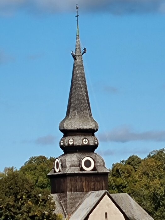 Historisk kyrkobyggnad, traditionellt torn, karakteristisk spira, blå himmel, trästruktur, rundade fönster.