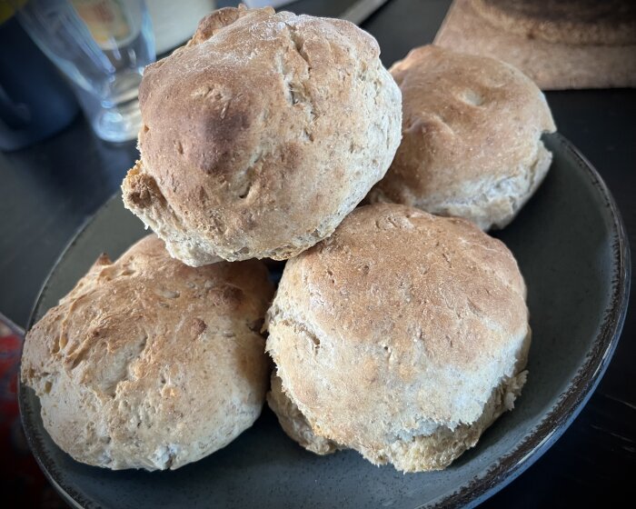 Fem nybakade bruna runda bröd på en mörk tallrik, hemgjorda, rustika, bakgrund suddig.