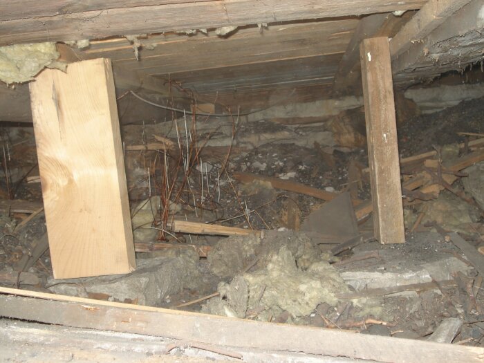 Gamla träbjälkar, isoleringsmaterial, skräp, förfall under golv. Behov av reparation eller renovering. Dusty, övergivna utrymmet.