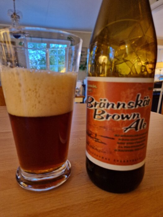 Ett glas fyllt med öl och en ölflaska märkt "Brown Ale" på ett bord.