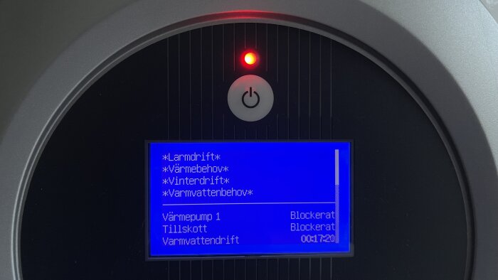 Digital kontrollpanel för uppvärmningssystem med röd varningslampa och blåskärm med text på svenska.