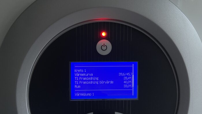 Digital display visar temperaturdata, möjligen för en värmepump eller termostat, innefattar påslagen symbol och röd lampa.