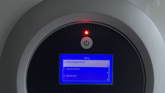Digital kontrollpanel med meny för rumstemperatur, varmvatten och semesterläge, röd strömindikator tänd.