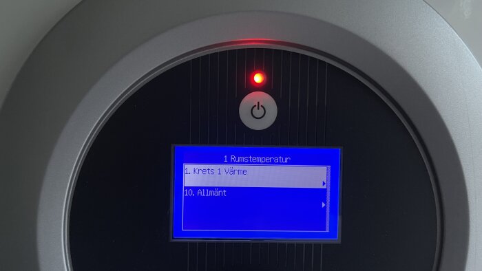 Digital display med blå bakgrund, menyval för rumstemperatur och värmeinställningar, röd indikatorlampa, av/på-knapp.