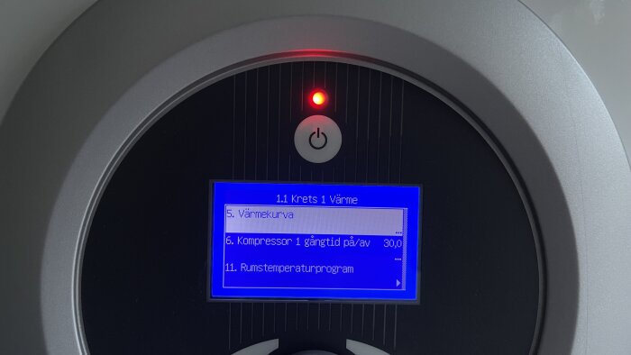 Digital kontrollpanel med blå skärm, röd indikatorlampa, på/av-knapp, svenska menyalternativ för värmesystem.