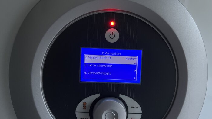 Värmesystemkontroll med display, knappar och rött ljus, menyn visar varmvatteninställningar, grå bakgrund.
