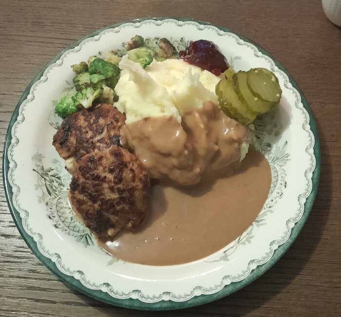 Ett måltid med köttbullar, potatismos, brunsås, lingonsylt, pickles och brända broccolibitar på ett dekorerat fat.