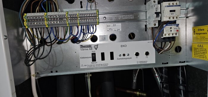 Elektrisk kopplingsskåp, kablar, kylbärarpumpsknapp, överspänningsskydd, varningslappar, värmepumpsutrustning, installationsdatum och signatur.