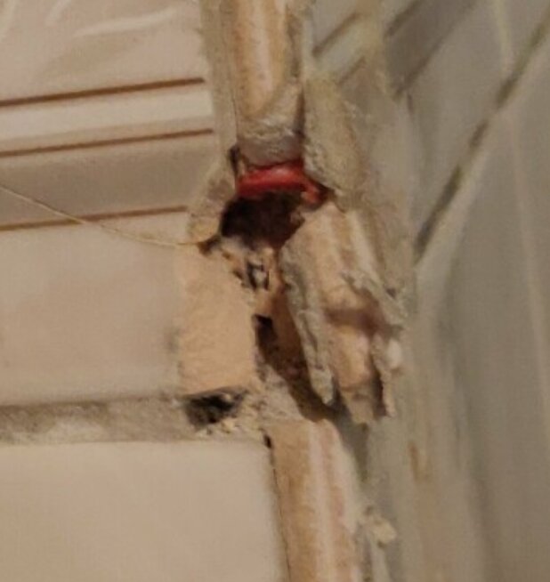 Närbild på skadat vägguttag: sprucket puts, exponerad röd isolator, synlig installation, behov av reparation.