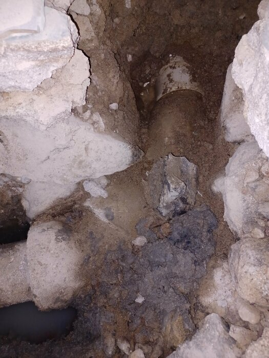 Ett grävt hål visar trasigt rör och uppbrottet betong, tyder på reparation eller vattenledningsarbete.