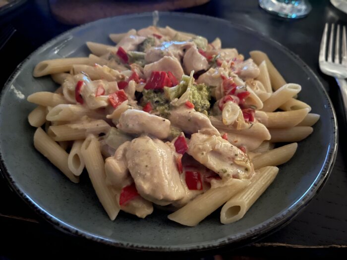 Tallrik med pasta, kyckling, broccoli och röd paprika i krämig sås. Serverad hemma.