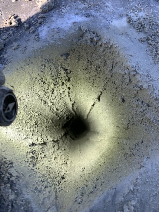 Ett hål i frusen yta med utstrålande sprickor, närbild, kanske asfalt, med oklart föremål ovanför.