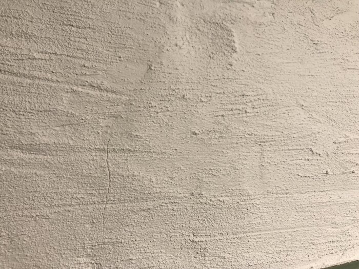 En texturerad vit vägg med skrapsår och små oregelbundenheter.
