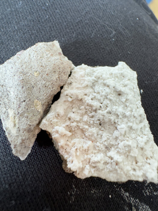 Två oregelbundna bitar av porös sten på en svart vävtextil. Varierande textur och färg. Geologi eller byggmaterial.